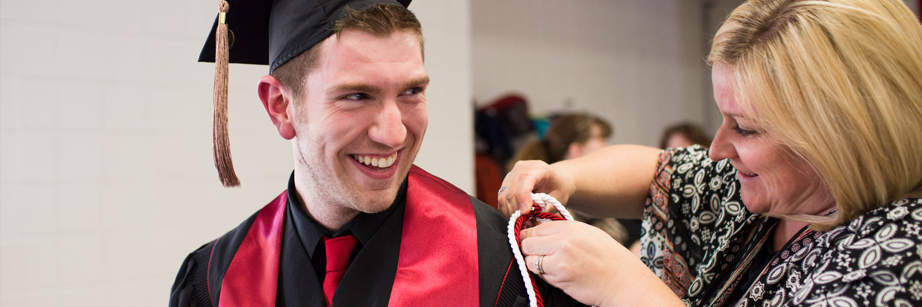 A woman helps a business graduate pin his honor cords to his graduation robe