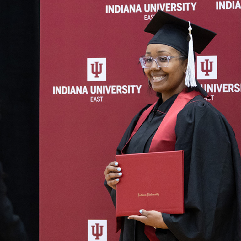 A proud graduate poses with her diploma in front of an IUE backdrop