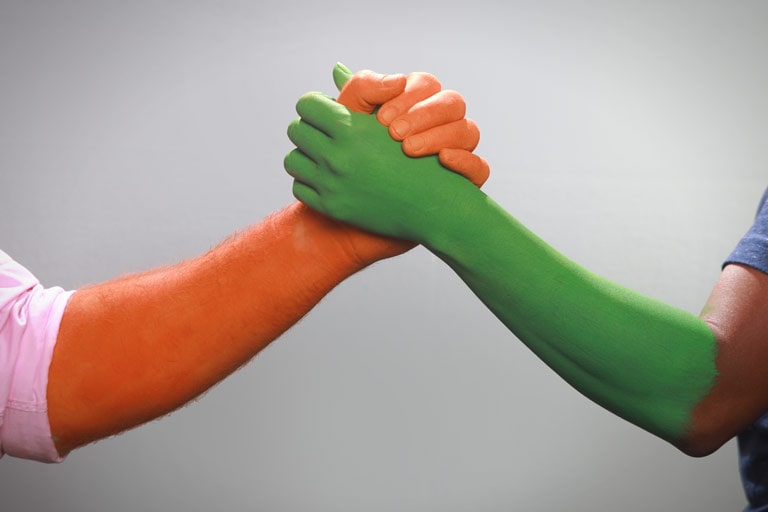 Two arms, one painted orange and the other green, joining hands in solidarity.
