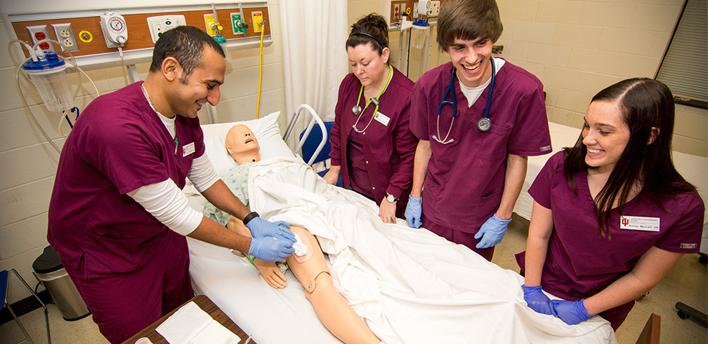 Nursing students bonding and laughing while performing procedure on medical dummy.