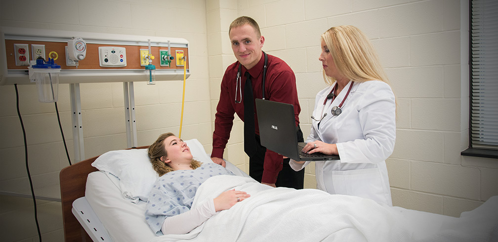 Tyler Evans smiling and working with female patient on hospital bed.
