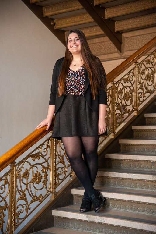 Caysey smiling and standing on the ornate staircase inside the Rush County courthouse.