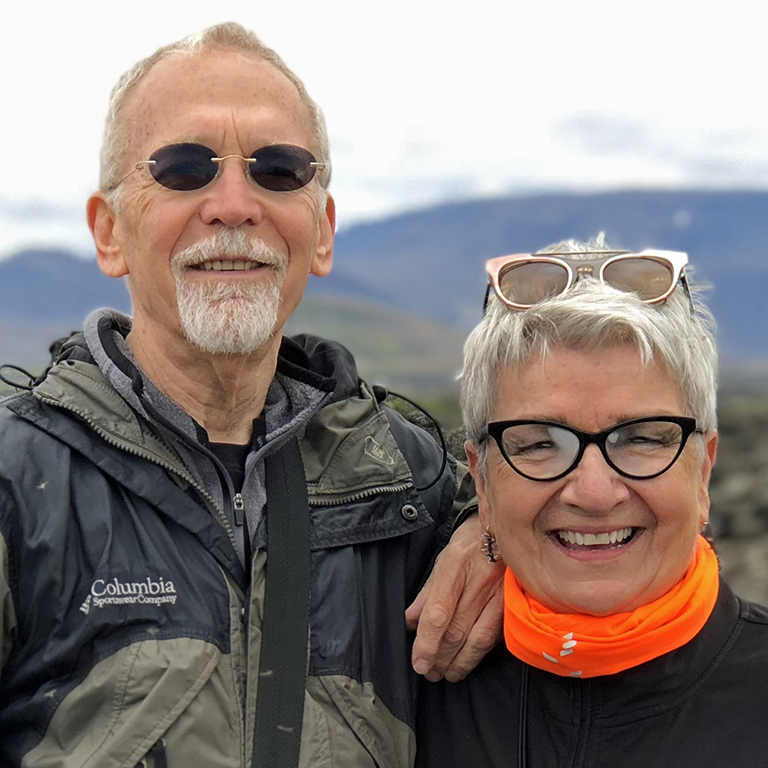 Jerry Logan stands next to his wife Terri Logan in front of a mountain landscape