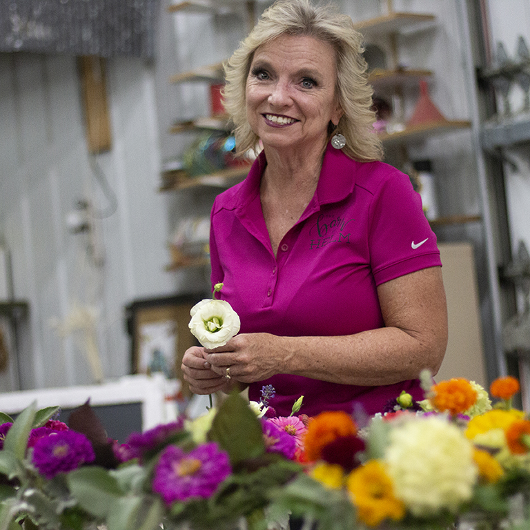 woman stands smiling holding a flower