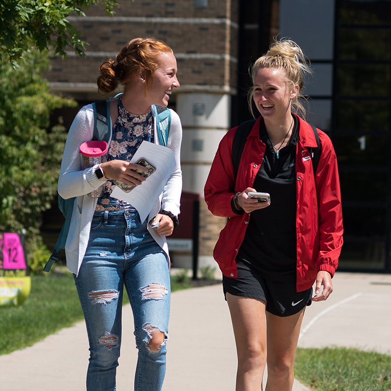 Photo of two girls walking together on the IU East campus in front of a building in the quad.