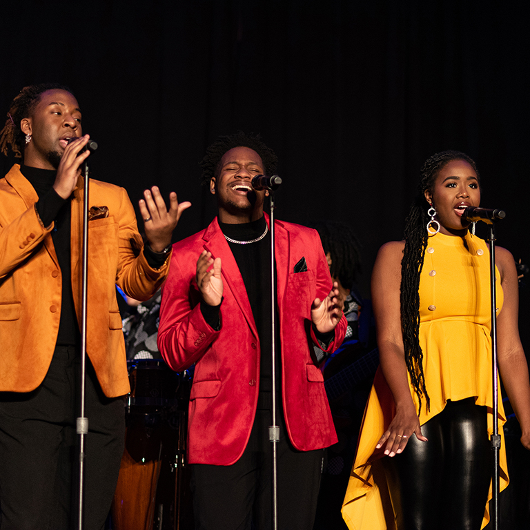 Male singers in velvet red and orange suit coats and female singers in yellow tunics.