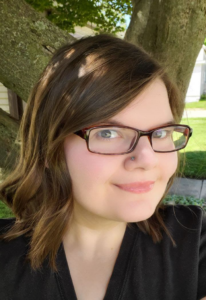 A girl with brown, curly, shoulder-length hair wearing glasses and a black shirt.